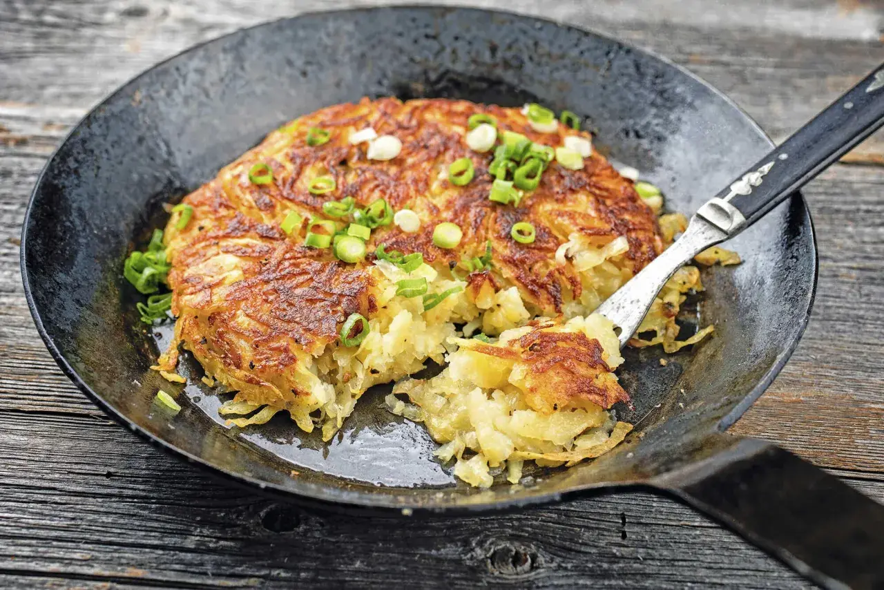 Herzhaft gebratene Kartoffelpuffer, perfekt für Meal Prep Kartoffeln, garniert mit Frühlingszwiebeln in einer Gusseisenpfanne.