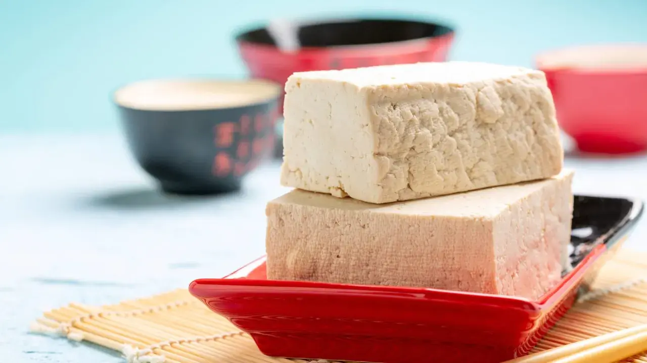 Zwei Blöcke Tofu auf einem roten Teller, bereit zum Genuss. Ja, man kann Tofu roh essen, er ist vielseitig!