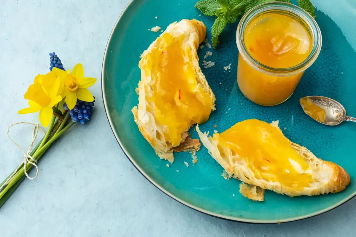Quittenrezepte Marmelade auf Brot, daneben ein Glas mit der leuchtend gelben Marmelade und ein Löffel. Ein Frühlingsstrauß mit Narzissen und Traubenhyazinthen.