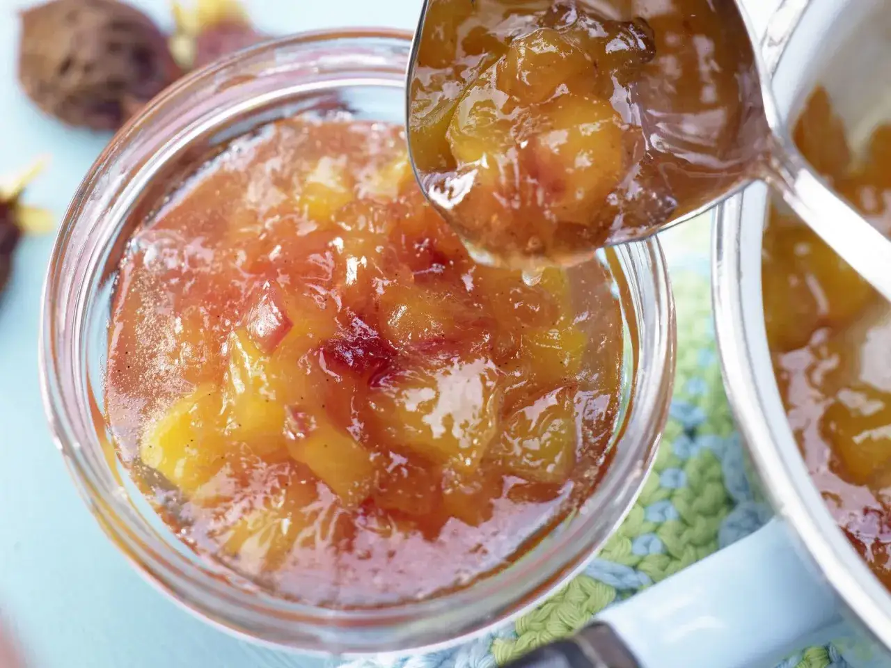 Ein L&ouml;ffel hebt gl&auml;nzende Nektarinen Marmelade aus einem Glas. Die Fruchtst&uuml;cke schimmern in der Sonne.