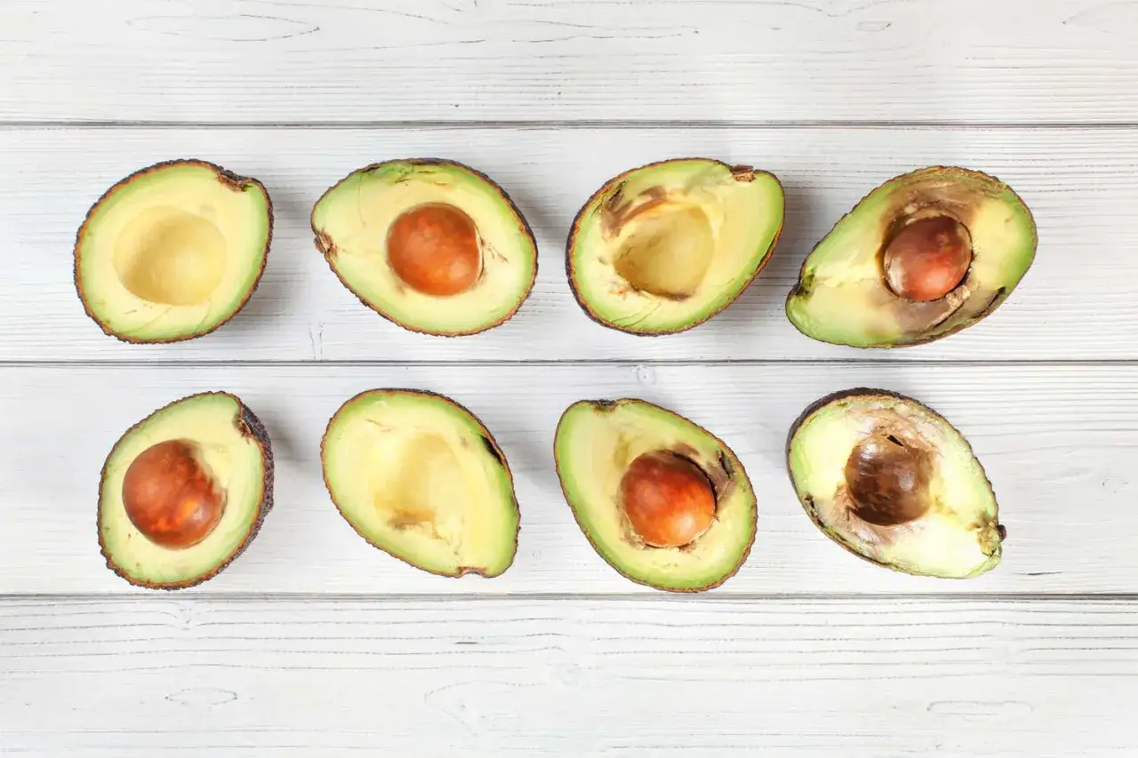 Acht halbierte Avocados liegen auf weißem Holz. Einige haben einen braunen Kern, andere sind innen braun.