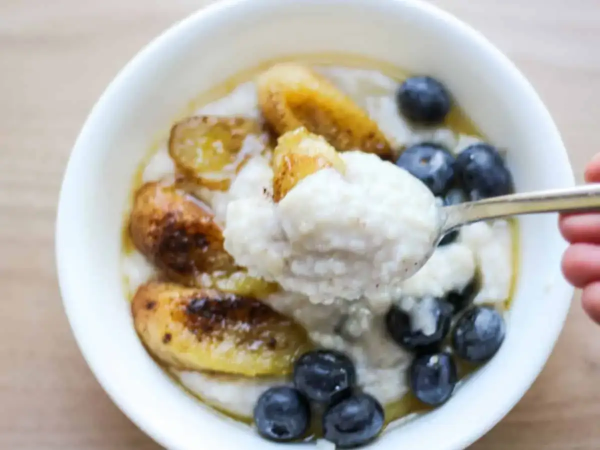 Cremiges Buchweizen Porridge mit karamellisierten Bananen und Blaubeeren, serviert in einer wei&szlig;en Sch&uuml;ssel. Ein L&ouml;ffel voller Genuss.