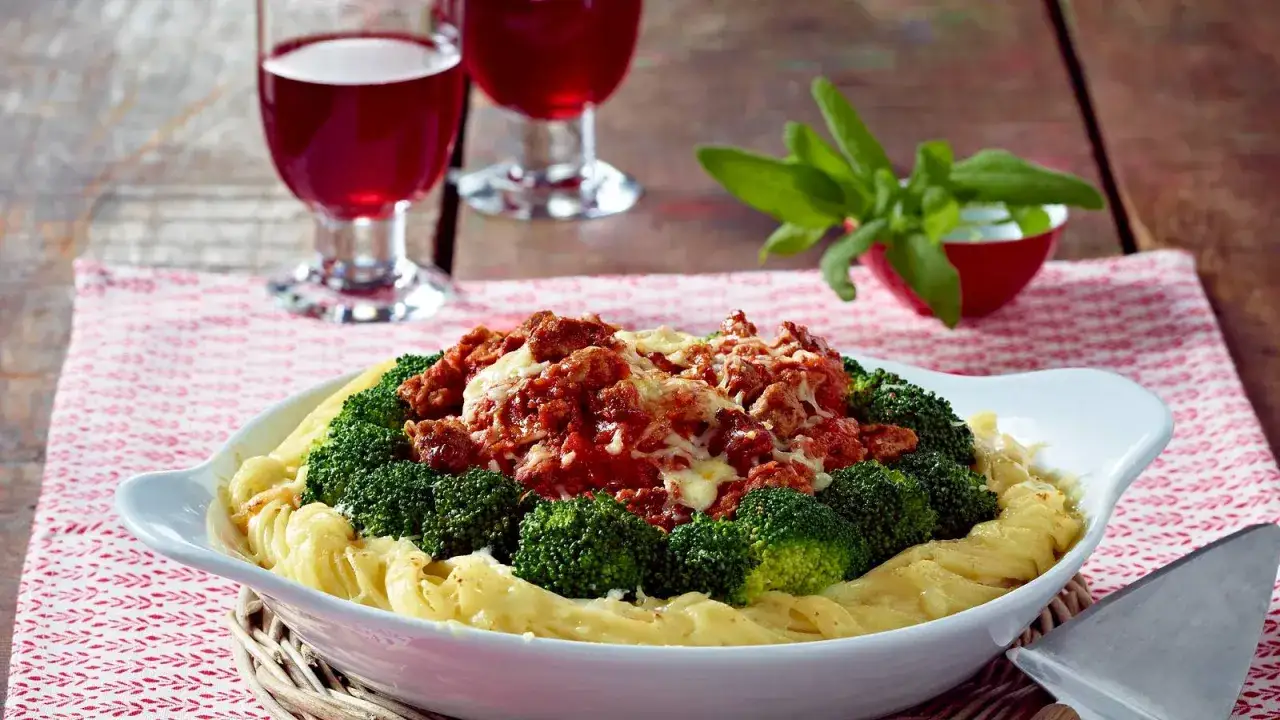 Herzhafte Brokkoli Bolognese mit geschmolzenem Käse auf Bandnudeln, serviert mit Rotwein.