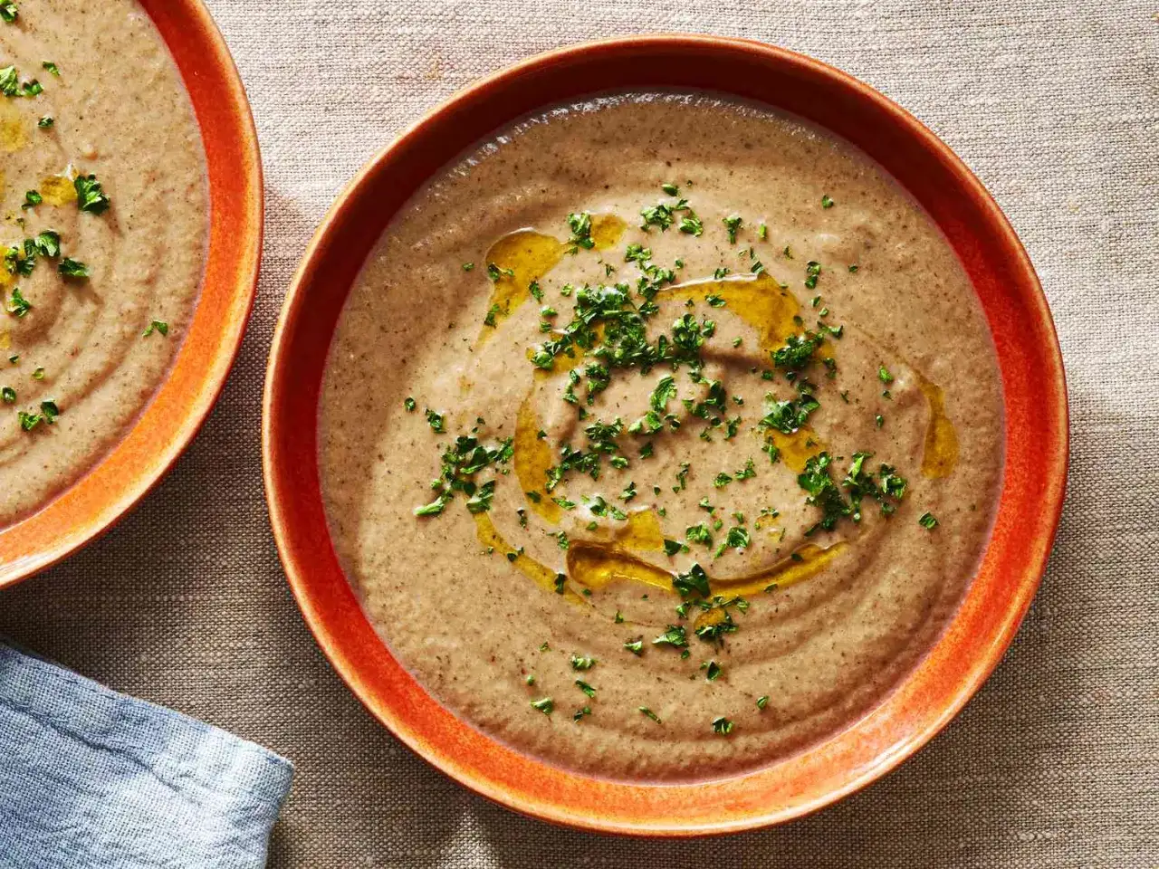 Zwei Teller cremiger Pilzsuppe, garniert mit Oliven&ouml;l und Petersilie, warten auf Genuss.