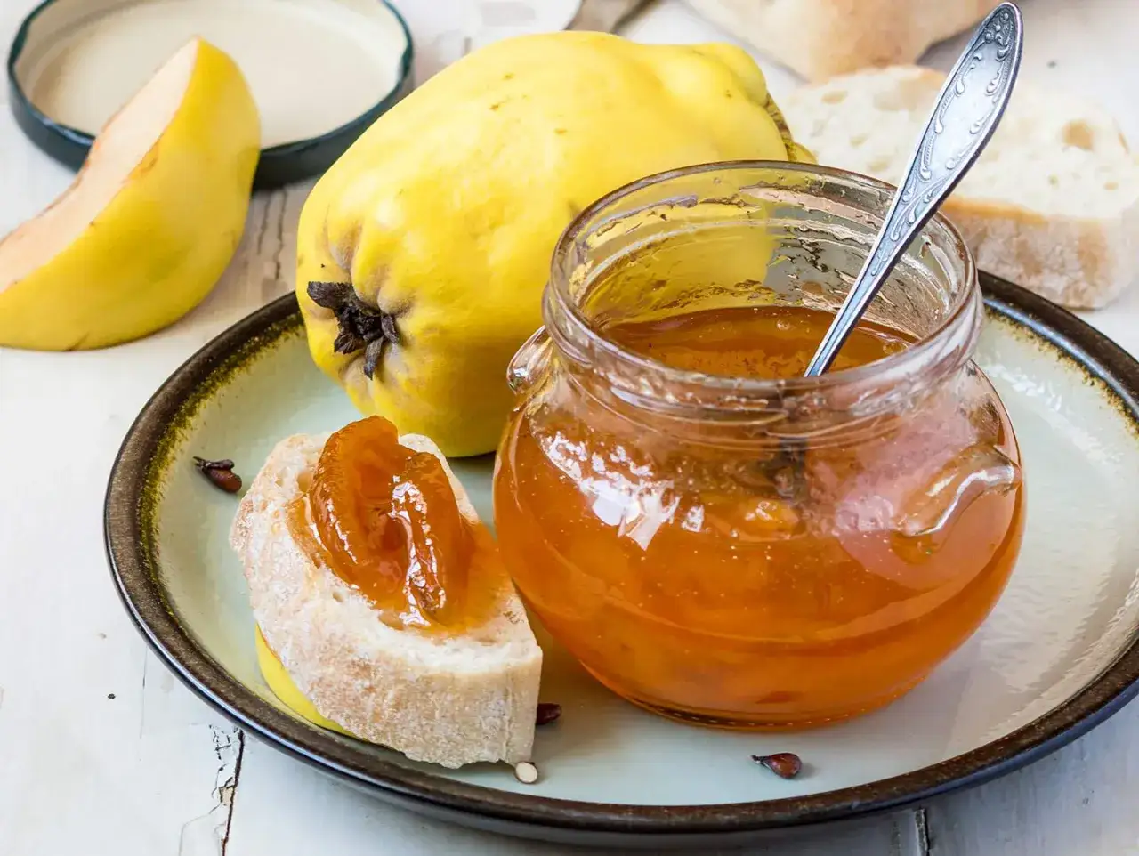 Quittenrezepte Marmelade: Ein Glas goldener Quittenmarmelade, daneben frische Quitten und ein St&uuml;ck Brot mit Marmelade.