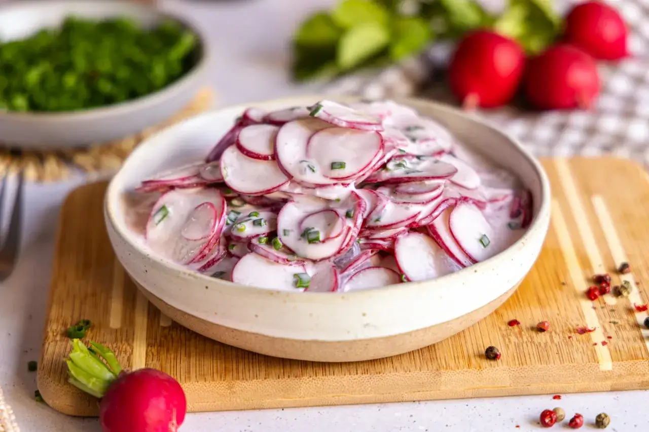 Frischer radieschensalat mit joghurt und schnittlauch, garniert mit pfefferk&ouml;rnern.