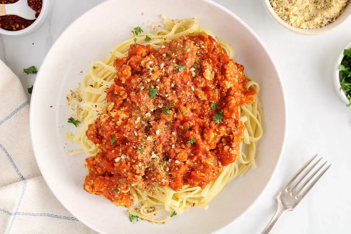 Herzhafte Tofu-Bolognese auf Bandnudeln, garniert mit Petersilie und veganem Parmesan.