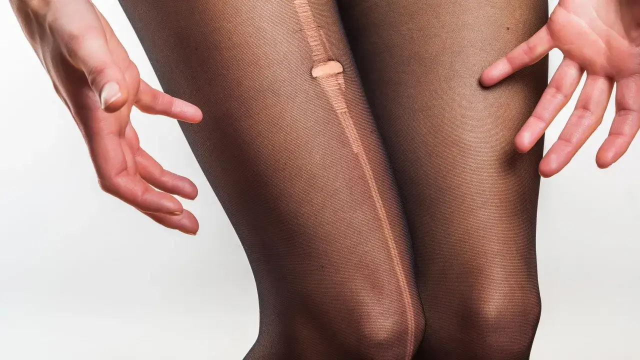 Hände zeigen ein Loch in einer schwarzen Strumpfhose, das zum Strumpfhose reparieren einlädt.