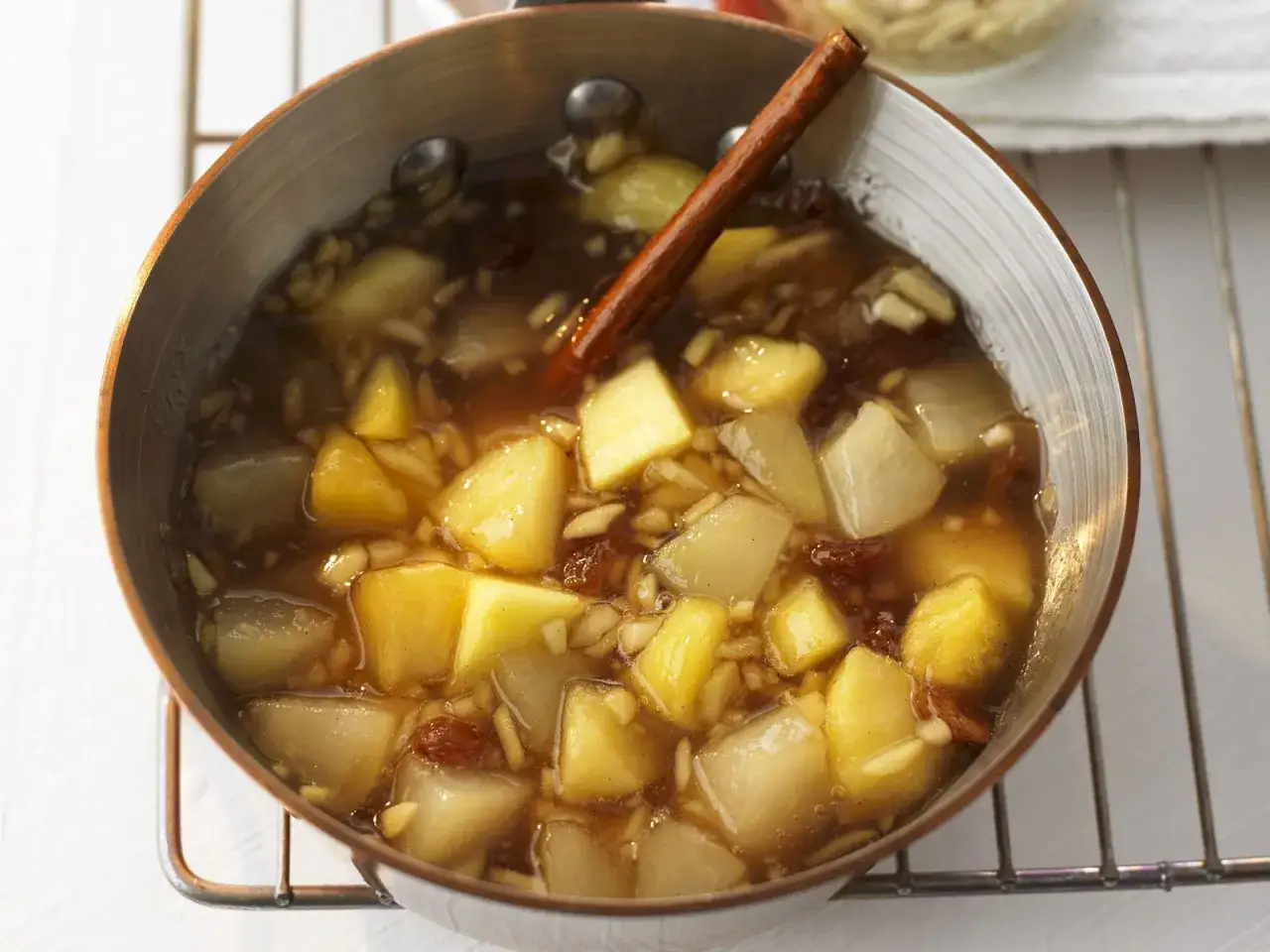 Ein Topf mit warmem Apfel-Birnen-Kompott, verfeinert mit Zimtstange, Rosinen und Mandelsplittern.