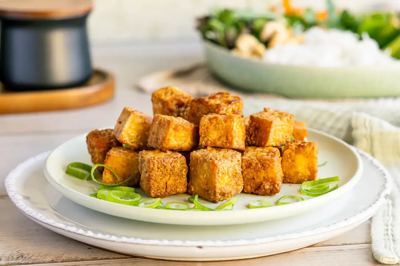 Goldbraun gebratene Tofuw&uuml;rfel, perfekt zum tofu zubereiten, garniert mit Fr&uuml;hlingszwiebelringen auf einem Teller.
