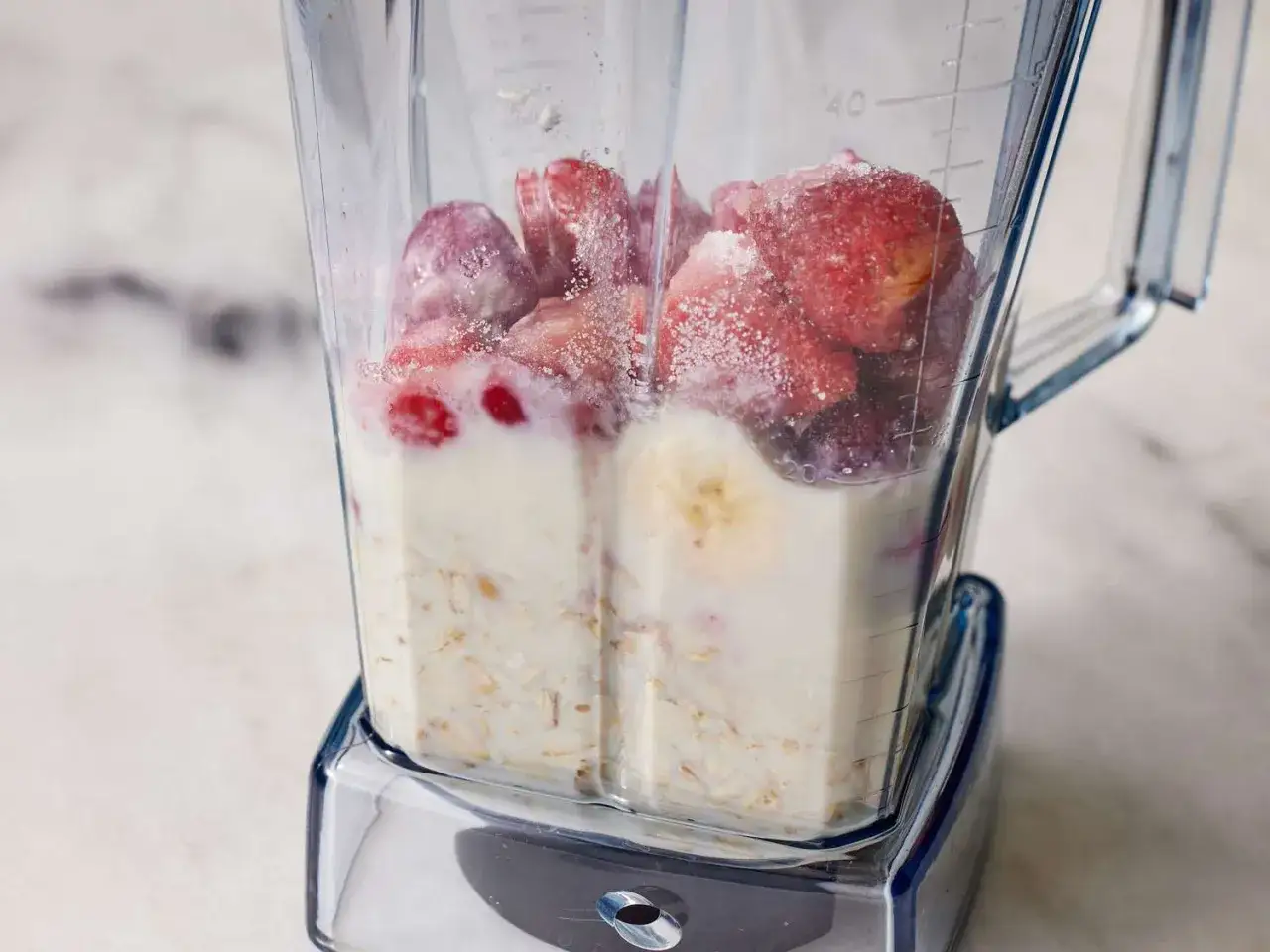 Ein Mixer mit gefrorenen Erdbeeren, Banane, Milch und Haferflocken f&uuml;r einen gesunden smoothie mit haferflocken.