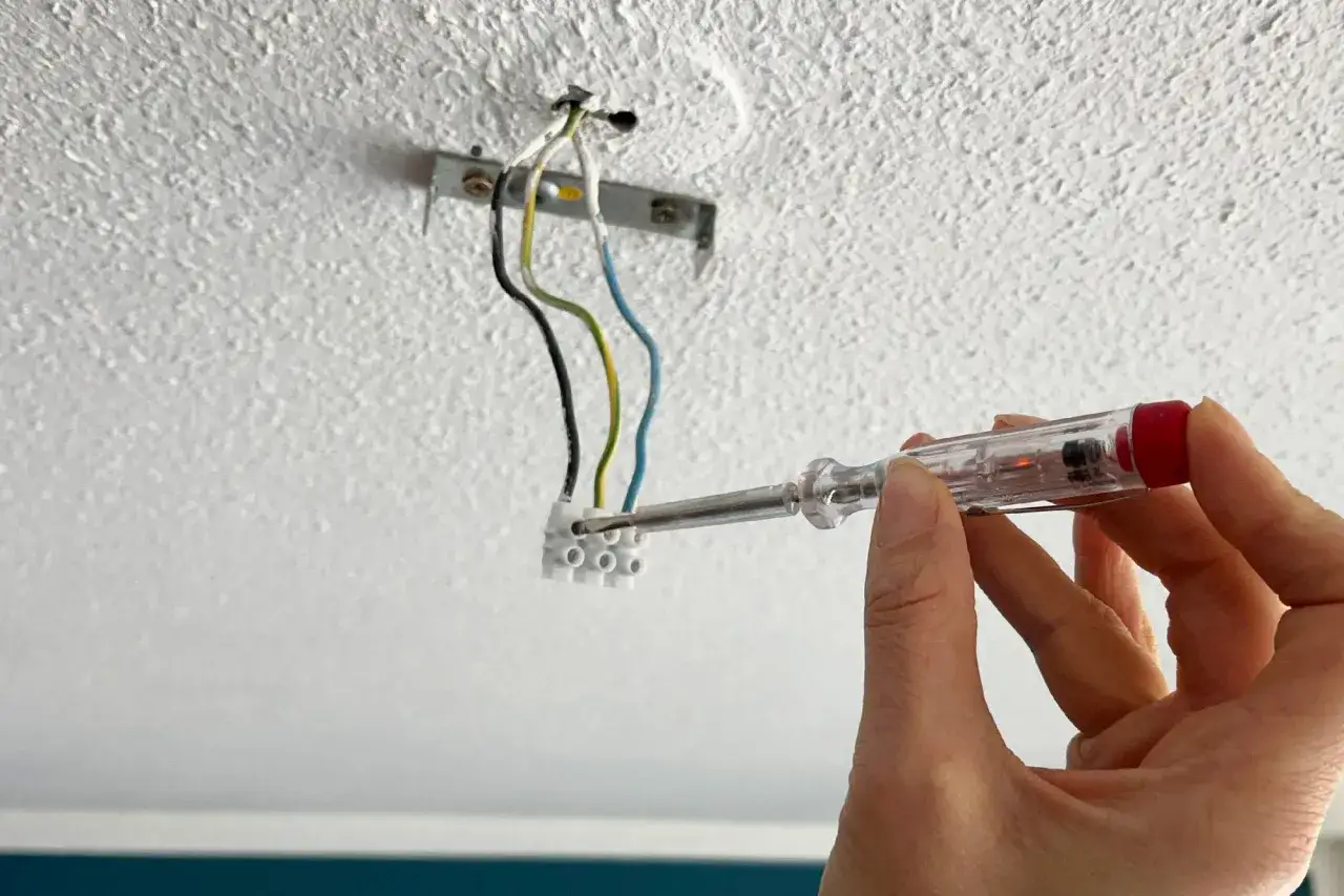 Hand uses a voltage tester to check wires before attaching a lamp to the ceiling.