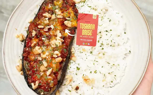 Gefüllte Aubergine mit einer würzigen Tofu-Bolognese-Mischung, garniert mit Walnüssen und Petersilie, serviert mit Reis.