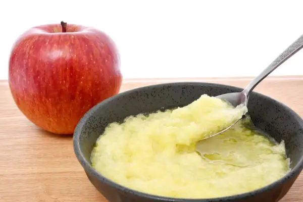 Ein roter Apfel neben einer Schüssel mit Apfelmus, ideal bei Magen-Darm-Beschwerden.