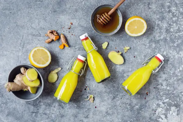 Zutaten für ein Ingwer Shot Rezept: frischer Ingwer, Zitrone, Honig und drei Flaschen des gelben Shots.