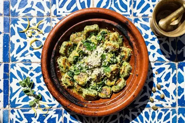 Spinat Ricotta Gnocchi, garniert mit Parmesan und Zitrone, serviert in einer Terrakotta-Schale auf blau-weißen Fliesen.