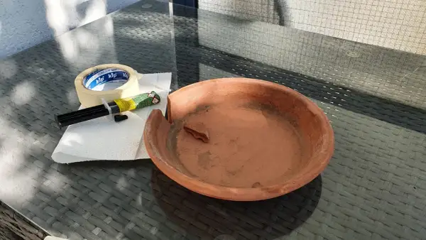 Zerbrochener Tontopf, Kleber und Klebeband liegen bereit, um den Schaden zu beheben.