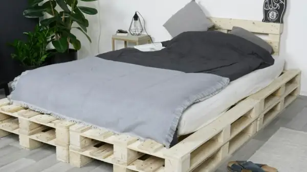 Ein rustikales Bett, das man einfach selber bauen kann, aus Europaletten. Mit grauer Decke und Kissen.