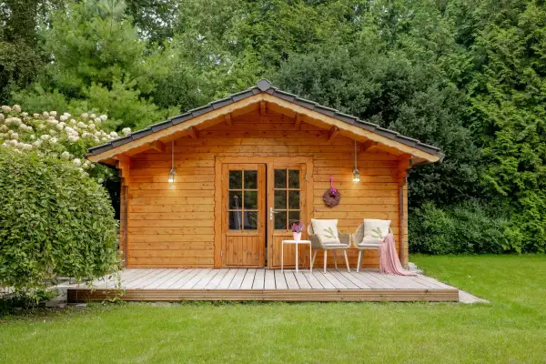 Ein gemütliches Gartenhaus, das man gut selber bauen kann, mit Veranda, zwei Stühlen und einer Tür.