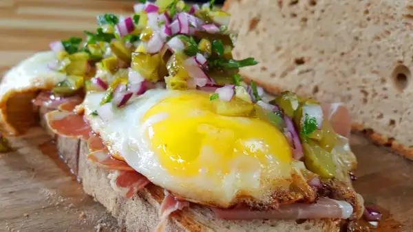Ein **strammer Max vegetarisch** mit Spiegelei, Schinken, Gewürzgurken und Zwiebeln auf rustikalem Brot.