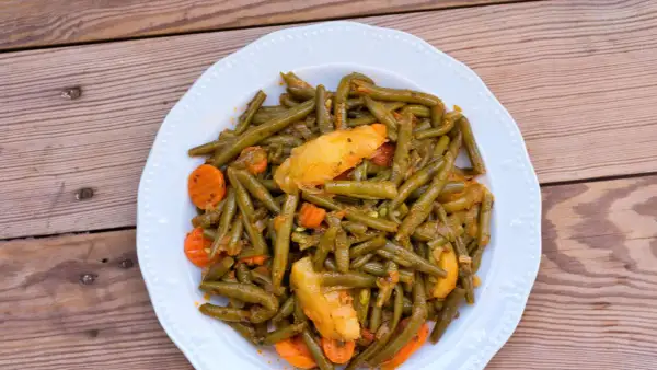 Ein Teller mit einem köstlichen Fasolakia Rezept, das grüne Bohnen, Kartoffeln und Karotten in einer würzigen Sauce zeigt.