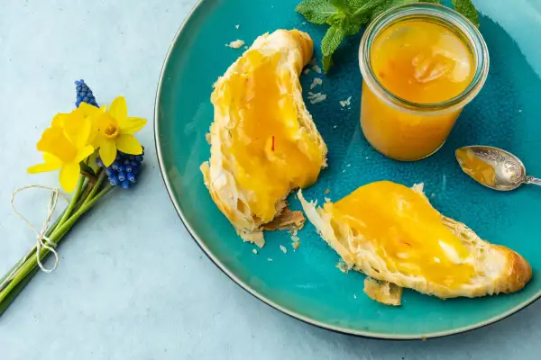 Quittenrezepte Marmelade auf Brot, daneben ein Glas mit der leuchtend gelben Marmelade und ein Löffel. Ein Frühlingsstrauß mit Narzissen und Traubenhyazinthen.