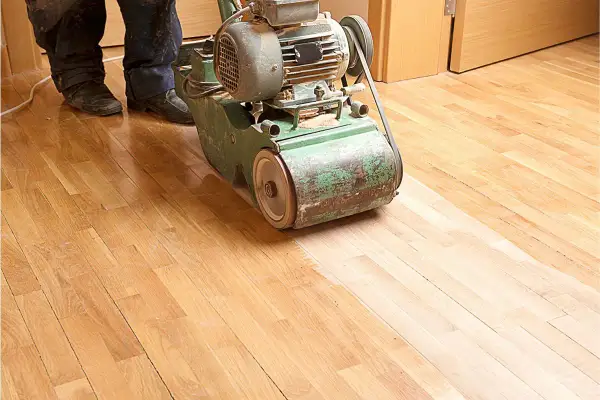 Ein Handwerker bearbeitet mit einer Schleifmaschine einen Holzboden. Das Parkett abschleifen erweckt den alten Boden zu neuem Glanz.