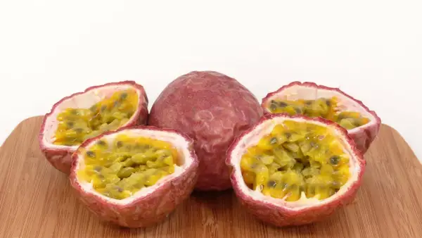 Ein ganzes und vier halbierte Passionsfrüchte liegen auf einem Holzbrett. Die Fruchtkerne sind saftig und gelb. Perfekt zum Passionsfrucht essen!