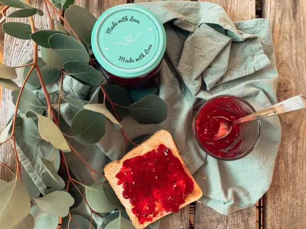 Glas mit Johannisbeermarmelade ohne Gelierzucker, daneben ein Toast mit Marmelade und ein Löffel.