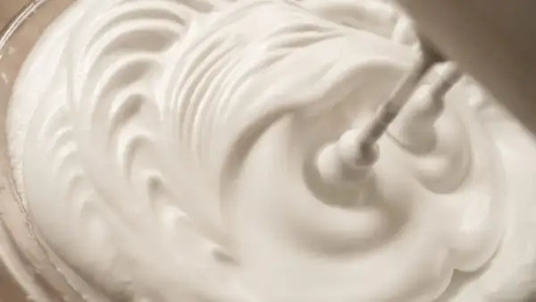 Sahne steif schlagen ohne Sahnesteif: Ein Handmixer formt cremige Wellen in der weißen Masse.